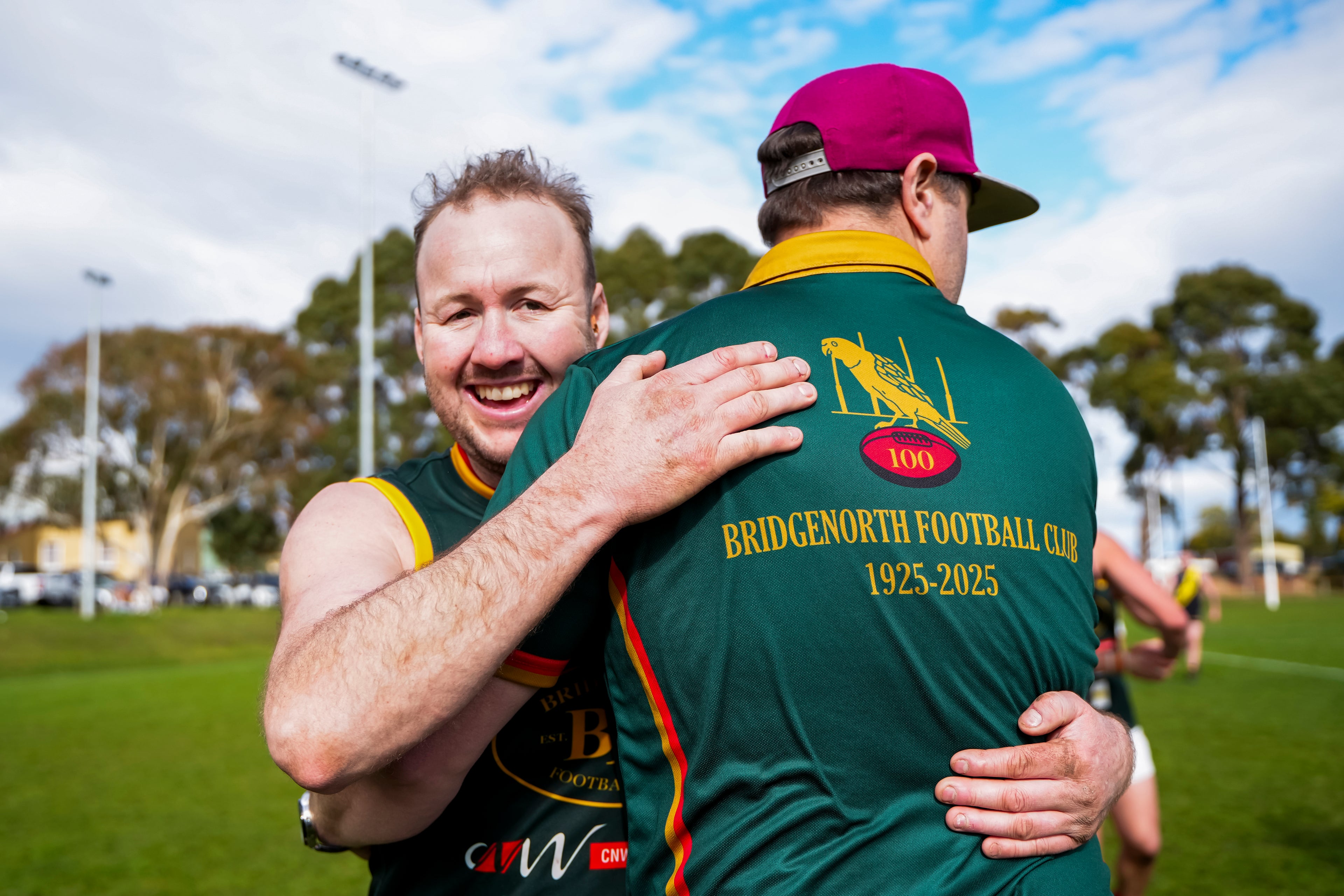 Two men celebrating on a sports field with one wearing a Bridgnorth Football Club polo