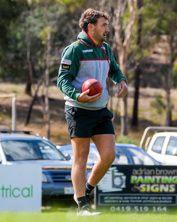 James Griffits in Bridgenorth Football Club clothes holding the football on a grassy field with cars and signs in the background